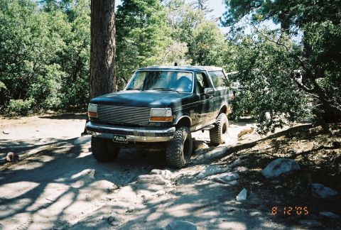 1990 Ford Bronco - black lifted Ford Bronco with a billet grille sits on a shaded dirt trail among pines, dated August 2005.