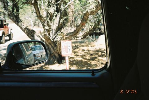 1990 Ford Bronco - Through a vehicle window, a side mirror reflects another truck beside a trail sign on a wooded path, dated August 2005.