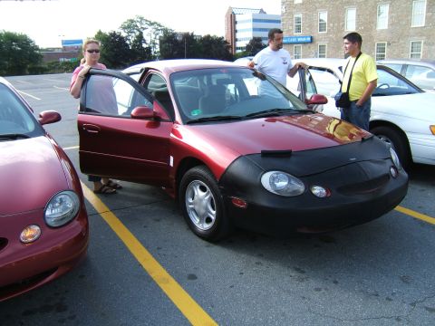 1998 Ford Taurus - A red 1998 Ford Taurus is parked in a lot with its doors open, next to another red vehicle.