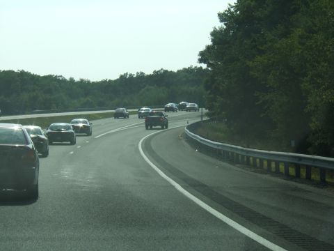 1998 Ford Taurus - A convoy of vehicles travels down a highway under a bright sky, with trees lining the roadside.
