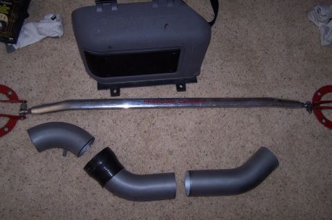 1997 Ford Probe - Car parts including a strut bar and intake piping laid out on a carpeted surface.