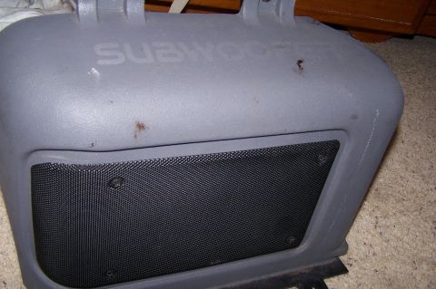 1997 Ford Probe - A gray plastic subwoofer enclosure with a black mesh speaker cover is visible, along with embossed text on its surface.