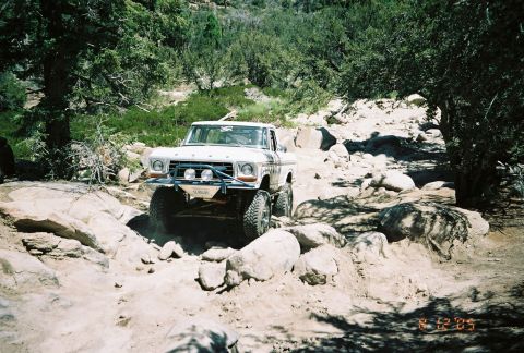 1990 Ford Bronco - white lifted vintage pickup with auxiliary lights crawls up a rocky boulder-strewn trail, dated August 2005.