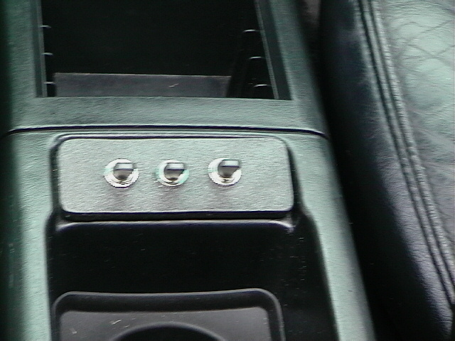 Close-up of three toggle switches mounted on a silver plate in a car's center console