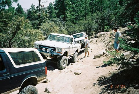 1990 Ford Bronco - Several lifted trucks line up on a narrow rocky trail as bystanders watch on the bank, dated August 2005.