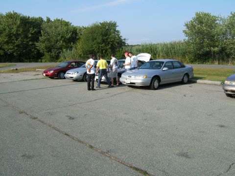 1998 Ford Taurus - Several cars and people gathered in a parking lot on a sunny day.