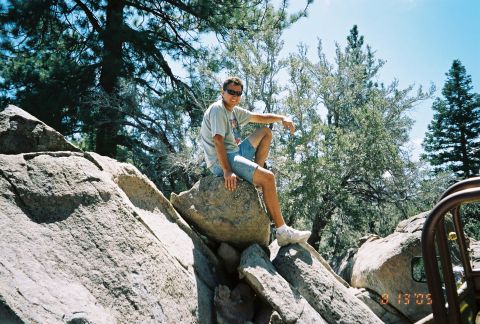 1990 Ford Bronco - man in sunglasses and shorts sits atop large granite boulders surrounded by pine trees, dated August 2005.