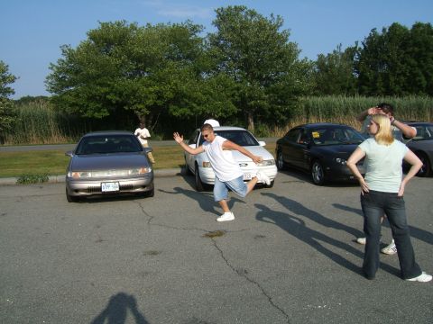 1998 Ford Taurus - A group of people stand around several cars in a parking lot on a sunny day.
