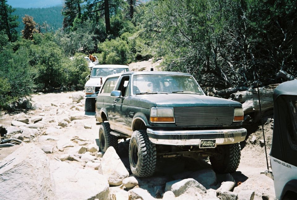 Lifted dark Ford Bronco on big tires parked on a rocky mountain trail with other 4x4s