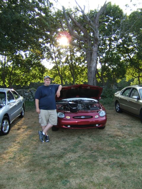 1998 Ford Taurus - A man poses with his red 1998 Ford Taurus at an outdoor car meet.