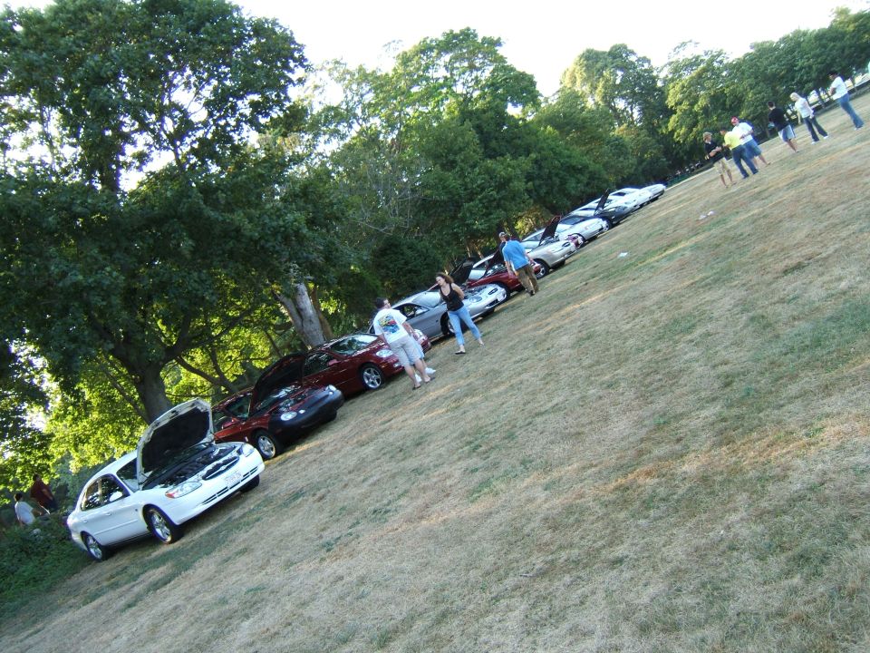 White sedan with hood open, parked on a grassy hill
