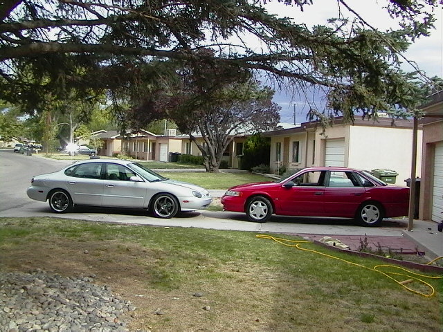 Silver 1999 Ford Taurus and red sedan parked side-by-side in driveway
