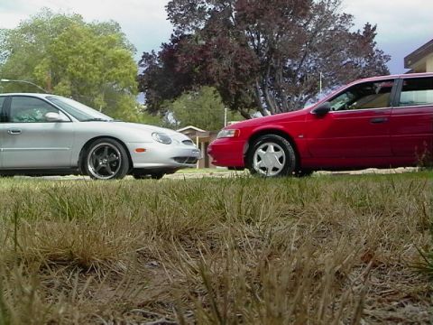 1992 Ford Taurus - Two sedans, one silver and one red, are parked on a grassy area with trees in the background.