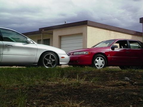 1992 Ford Taurus - Two sedans are parked closely together in front of a building with a garage door.