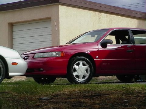 1992 Ford Taurus - A red 1992 Ford Taurus sedan is seen from the front three-quarter angle, parked beside another vehicle.