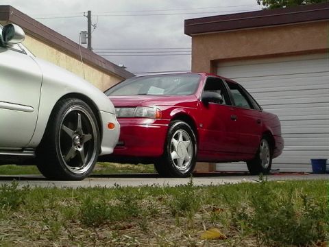 1992 Ford Taurus - Two cars parked in a driveway, one is a red 1992 Ford Taurus.