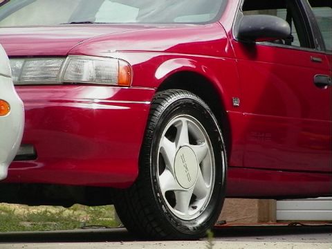 1992 Ford Taurus - A red sedan is parked next to a white vehicle, showing its front wheel and fender detail.