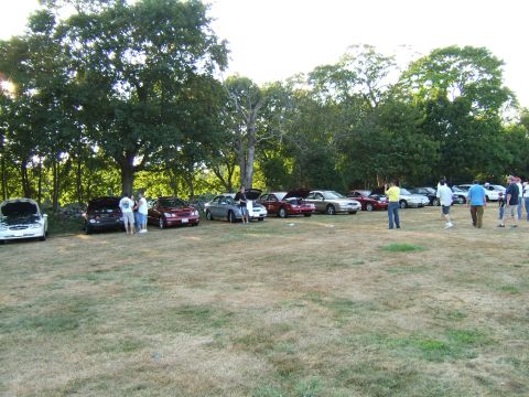 1998 Ford Taurus - A gathering of sedans parked on a dry, grassy field with trees in the background.