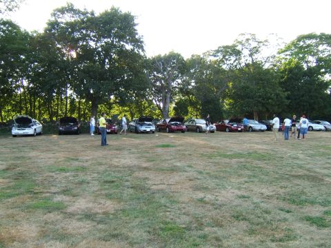1998 Ford Taurus - A gathering of vehicles and people in a grassy outdoor area, with several cars having their hoods open.