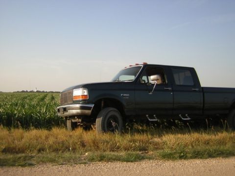 1996 Ford F-350 - A dark green 1996 Ford F-350 pickup truck is parked beside a field of tall green crops under a clear blue sky.