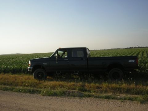 1996 Ford F-350 - Side view of a black 1996 Ford F-350 crew cab pickup truck parked next to a field of crops under a clear sky.
