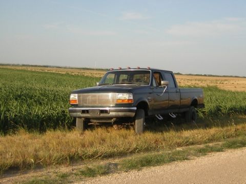 1996 Ford F-350 - Dark blue 1996 Ford F-350 crew cab pickup truck sits parked in a rural setting with fields on either side.