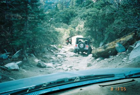 1990 Ford Bronco - Seen through a windshield, two Jeeps work down a rocky, tree-lined descent with a date stamp in the corner.