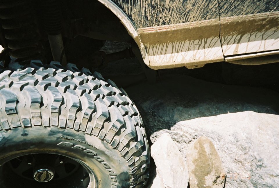 Close-up of a mud-splattered BFGoodrich off-road tire on a vehicle next to a large rock