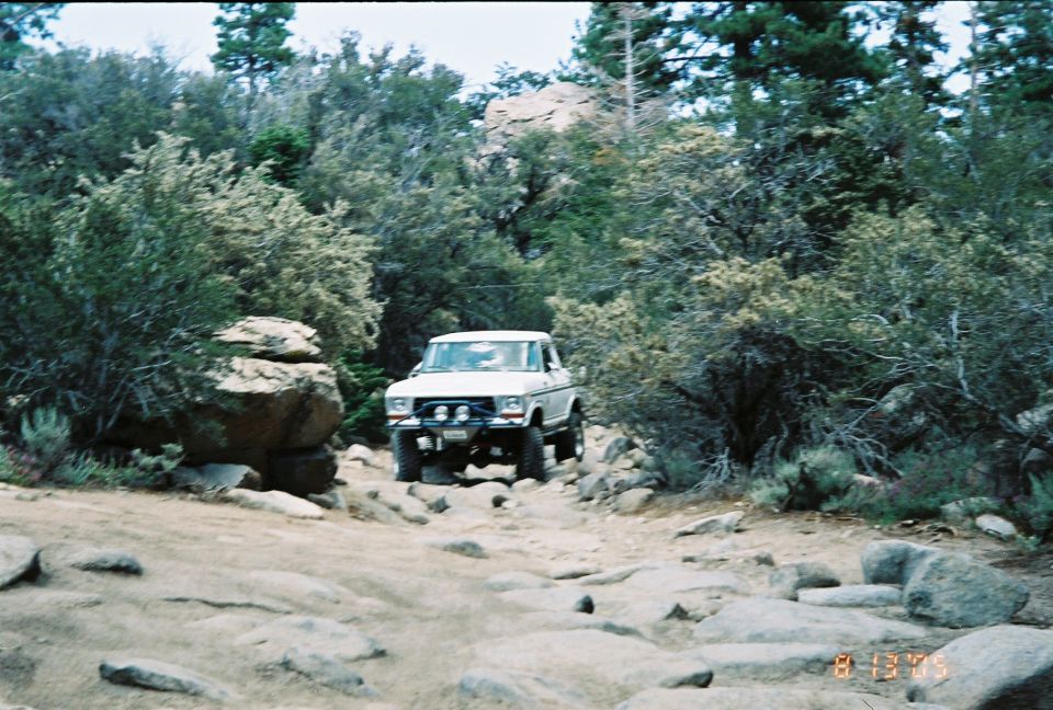 White lifted SUV on big tires parked on a dirt trail among desert brush and rocks