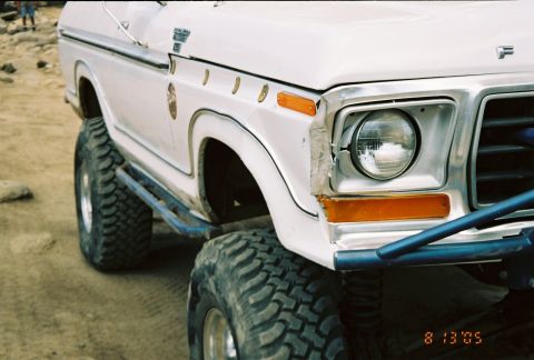 1990 Ford Bronco - Detail of a white lifted classic Ford truck showing a round headlight, chrome trim and an 'F' fender badge.