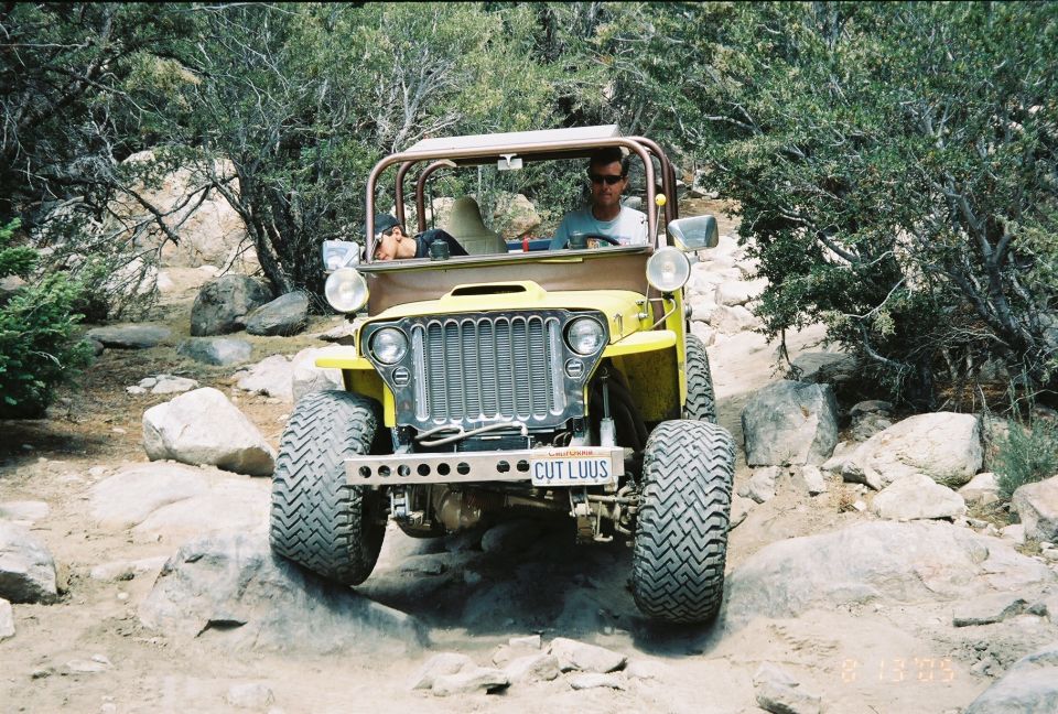 Yellow flatfender Jeep with roll cage and 'CUT LUUS' plate crawling over rocks