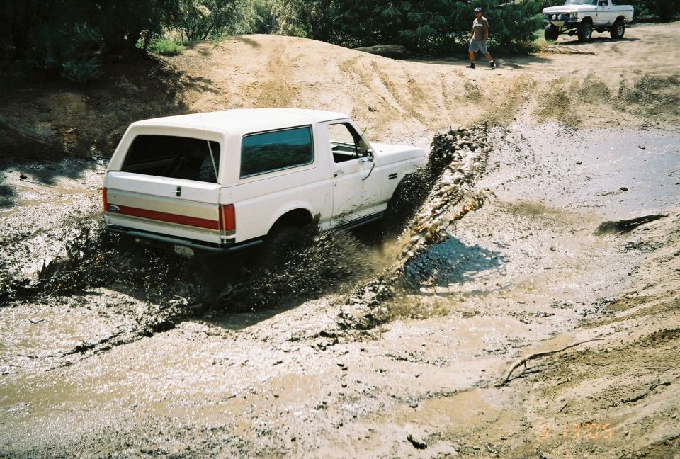 White SUV with red top driving through a muddy water crossing seen from above