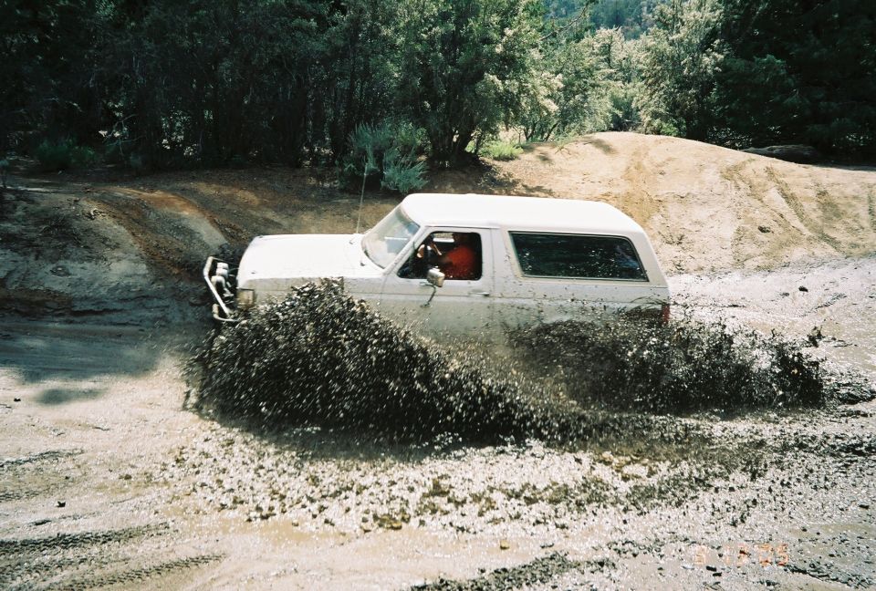 White SUV with red interior driving through a mud pit throwing a wide spray of mud