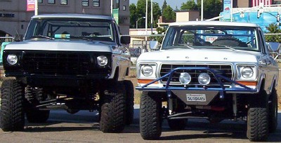 1995 Ford Bronco - Two modified Ford Broncos are parked side-by-side, displaying their lifted suspensions and off-road modifications.