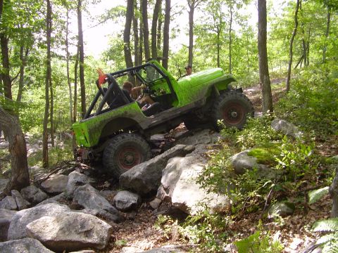 1995 Ford Bronco - A lime green open-top Jeep CJ/Wrangler with a black roll cage climbs a boulder-strewn trail through a hardwood forest, body flexed with the…