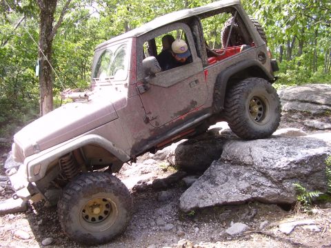 1995 Ford Bronco - A red Jeep Wrangler maneuvers over large rocks on an off-road trail.