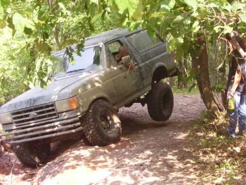 1995 Ford Bronco - A tan 1995 Ford Bronco navigates a challenging off-road trail, with one wheel lifted off the ground.