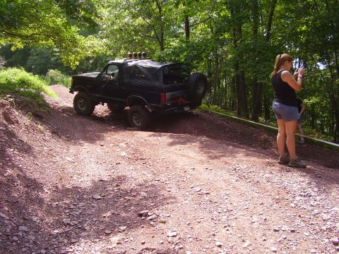1995 Ford Bronco - Black 1995 Ford Bronco navigates an off-road trail with a person taking photos.