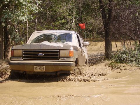 1995 Ford Bronco - A Ford Bronco navigates a muddy trail, its front tires submerged in water.