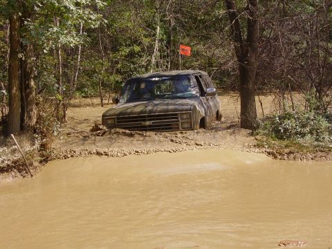 1995 Ford Bronco - An off-road vehicle is stuck deep in the mud, with only its front end visible above the brown water and dirt.