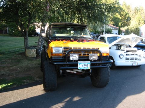 1991 Ford Explorer - A modified 1991 Ford Explorer with flame decals is parked next to another vehicle with its hood up.