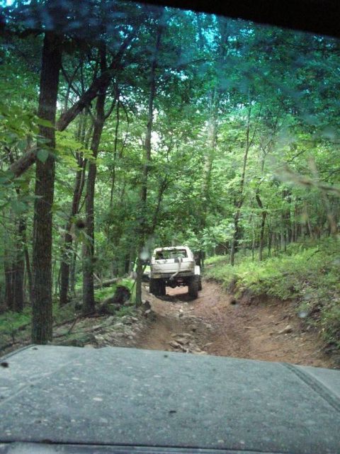 1995 Ford Bronco - A white 1995 Ford Bronco navigates a muddy trail through a dense forest.