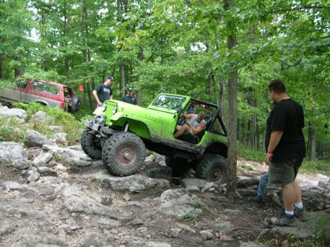 1995 Ford Bronco - Two off-road vehicles traverse a challenging rocky path in a wooded area.