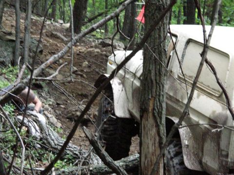 1995 Ford Bronco - A white 1995 Ford Bronco tackles a challenging off-road course through a dense forest, with a person visible near the front wheel.