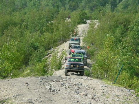 1995 Ford Bronco - Multiple off-road vehicles navigate a challenging dirt trail through a wooded area.