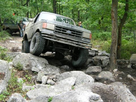 1995 Ford Bronco - A Ford Bronco is shown tackling a difficult off-road course with large rocks and trees.