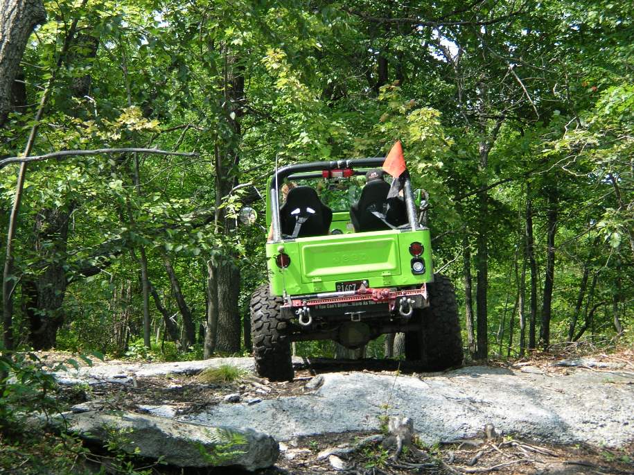Green off-road vehicle on a dirt path with trees in the background