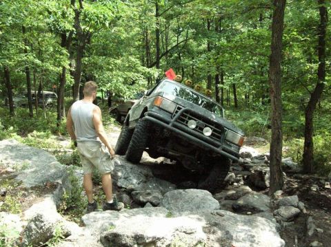 1995 Ford Bronco - A Ford Bronco is overturned in a wooded area, appearing to be stuck in a stream bed.
