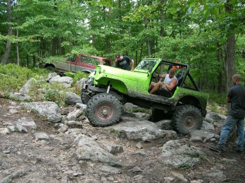 1995 Ford Bronco - Off-road vehicle tackling a challenging rocky trail surrounded by trees.