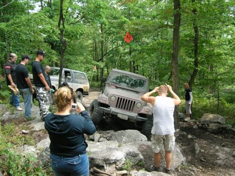 1995 Ford Bronco - A group of people observe an off-road vehicle as it traverses a rocky path in a wooded area.